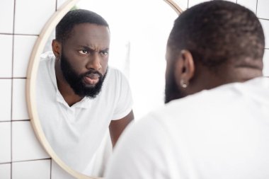 serious afro-american man looking at reflection in mirror clipart