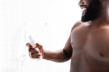 Elinde deodorant tutan gülümseyen Afro-Amerikan adam manzarası.
