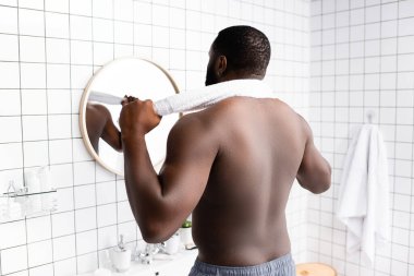 Boynunun arkasında havluyla aynaya bakan Afro-Amerikan bir adam. 