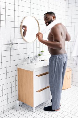 Tam boy gülümseyen Afro-Amerikalı adam banyoda, boynu arkasında havluyla dikiliyor. 