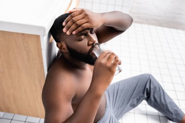 Afro-Amerikalı adam akşamdan kalma ve su içiyor.
