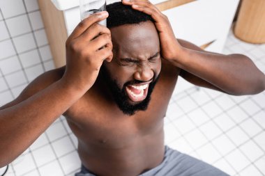 afro-american man screaming from headache and holding glass of water near temple clipart