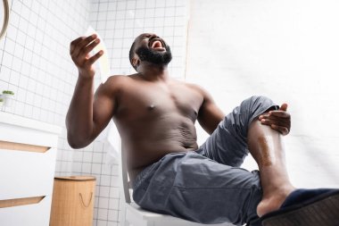 Afro-Amerikalı adam, balmumu şeritlerini yırtıyor ve acıdan bağırıyor. 