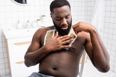 Afro-Amerikalı bir adam göğsüne balmumu bandı takıyor. 