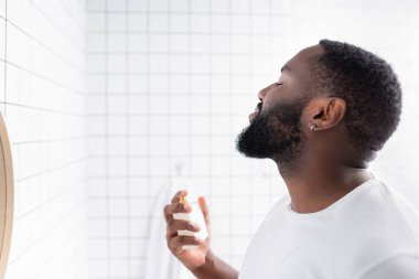 Beyaz tişörtlü Afro-Amerikan adam parfüm kullanıyor. 