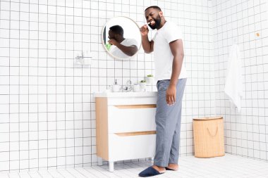 full length of afro-american man brushing teeth and looking back clipart