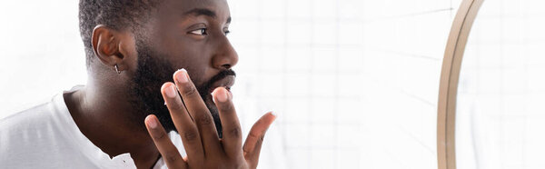 панорамный снимок афро-американского мужчины, применяющего лекарство для укрепления роста бороды