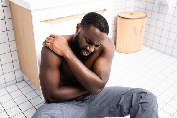 afro-american man sitting on bathroom floor and suffering from back pain