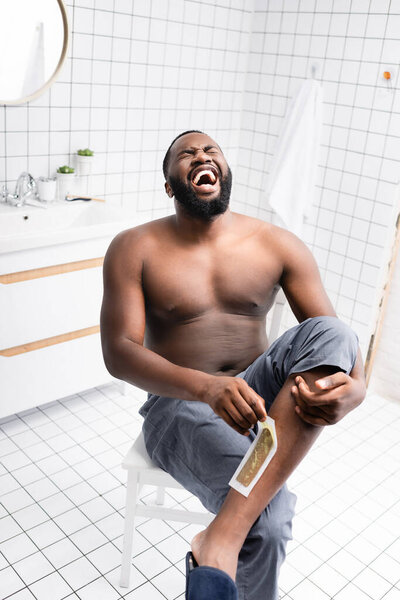 afro-american man tearing off wax strips and screaming from pain 