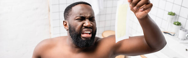 panoramic shot of afro-american man looking at wax strips with disgust