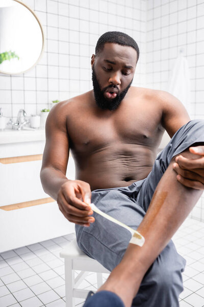 afro-american man tearing off wax strips from leg