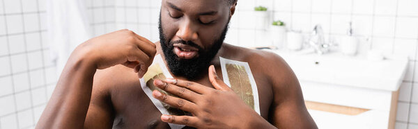 panoramic shot of afro-american man applying wax strips on chest 