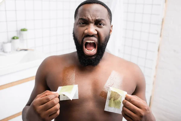 afro-american man tearing off wax strips and screaming from pain