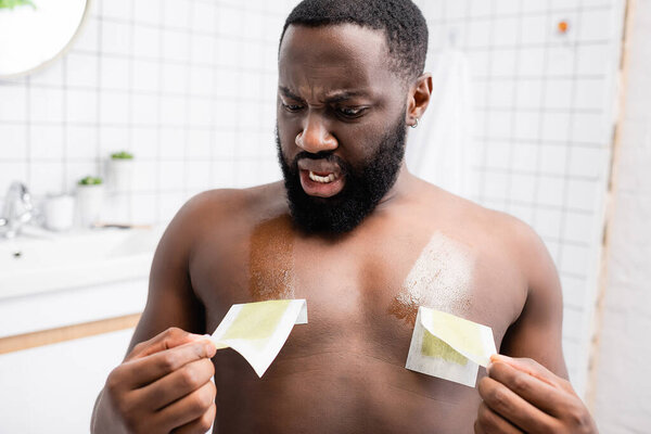 shocked afro-american man tearing off wax strips 
