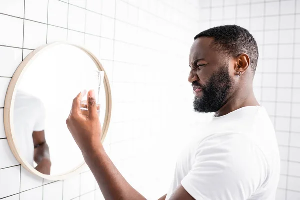 afro-american man grimacing from bad taste of water and holding glass in hand