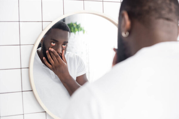 tired afro-american man pulling lower eyelids with fingers