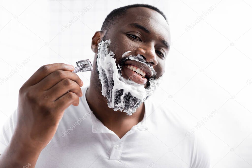 portrait of happy afro-american man shaving beard with razor 