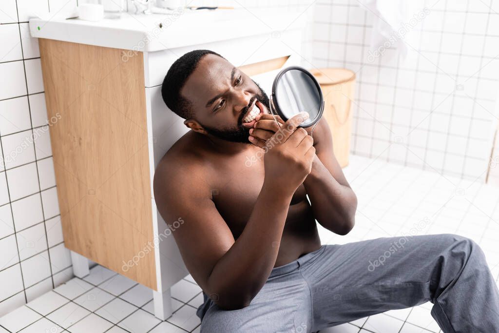 afro-american man sitting on bathroom floor and looking at gum in small mirror