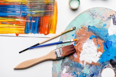 Gouache boyalarının üst görünümü, boya fırçaları ve beyaz arkaplanda kağıt üzerinde soyut renkli fırça darbeleri