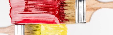 top view of paintbrushes near colorful red and yellow paint brushstrokes on white background, panoramic shot clipart