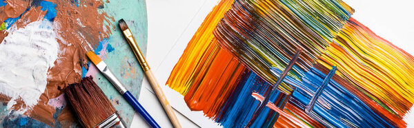top view of paintbrushes and abstract colorful brushstrokes on paper on white background, panoramic shot
