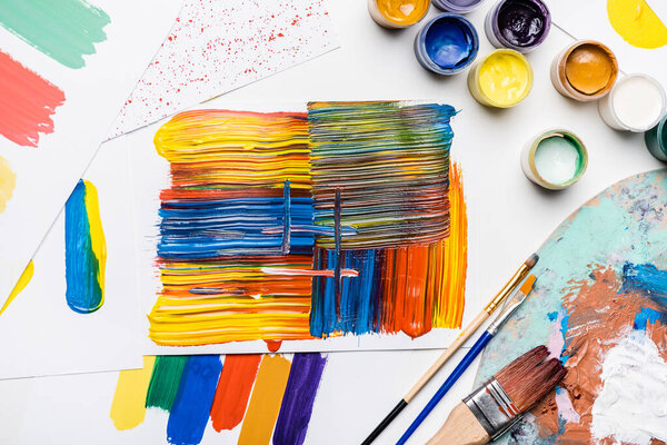 вид гуашь красок, кистей и абстрактных красочных мазков кисти на бумаге на белом фоне