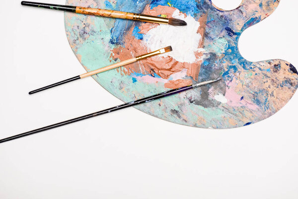 top view of palette with paints and paintbrushes isolated on white