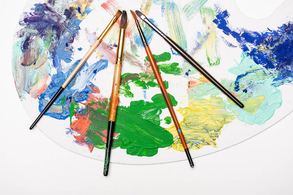 top view of palette with paints and paintbrushes isolated on white