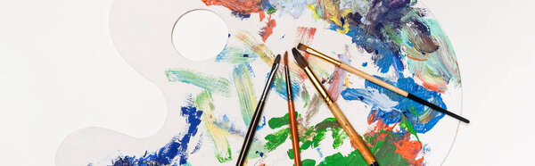 top view of palette with paints and paintbrushes isolated on white, panoramic shot