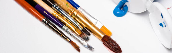 squeezed acrylic paints near paintbrushes on white background, panoramic shot