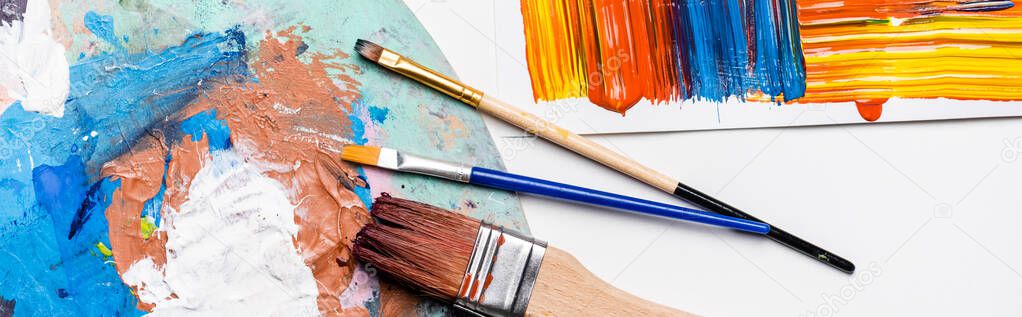 top view of paintbrushes and abstract colorful brushstrokes on paper on white background, panoramic shot