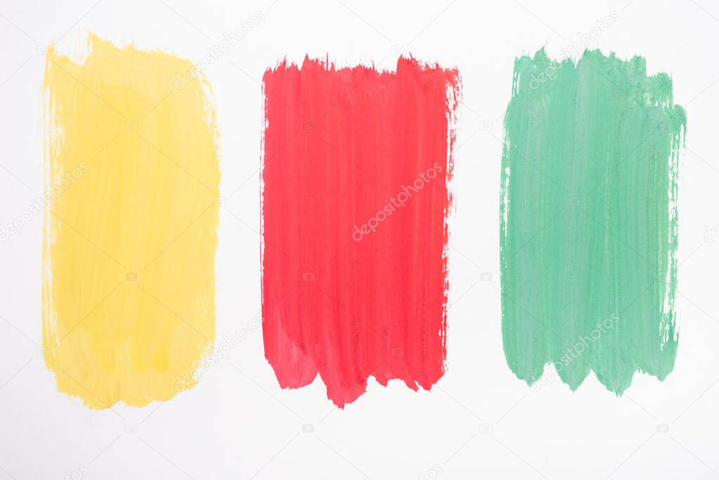top view of abstract colorful green, yellow and red paint brushstrokes on white background
