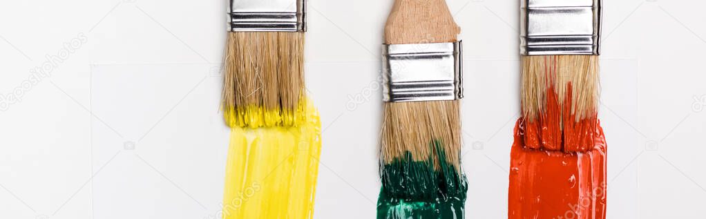 top view of paintbrushes near colorful paint brushstrokes on white background, panoramic shot
