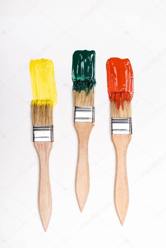 top view of paintbrushes near colorful paint brushstrokes on white background