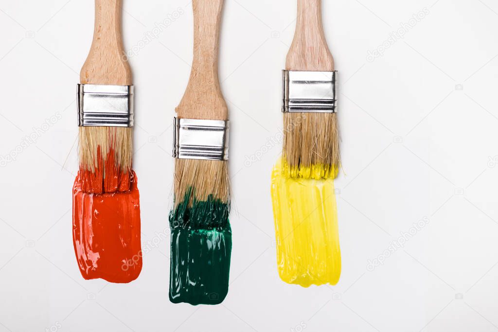 top view of paintbrushes near colorful paint brushstrokes on white background