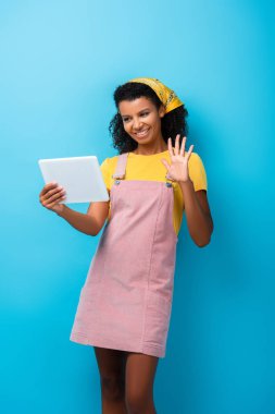 Mavi ekranda görüntülü arama yaparken başörtüsü sallayan mutlu Afro-Amerikalı kadın. 