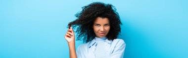 curly african american woman twirling hair on finger on blue, banner clipart