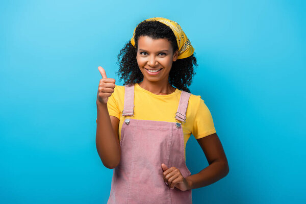 жизнерадостная африканская американка, показывающая большой палец на голубом