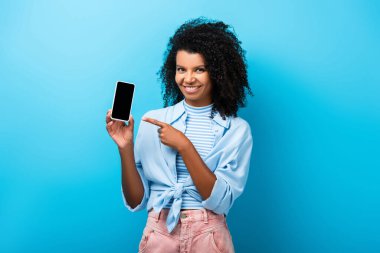 Mutlu Afro-Amerikalı kadın mavi ekranlı akıllı telefonu işaret ediyor.