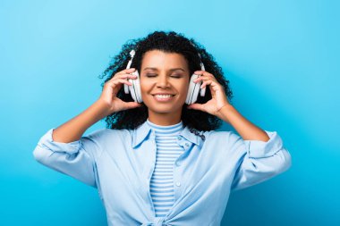 Mutlu Afro-Amerikalı kadın mavi kulaklıkla müzik dinliyor.