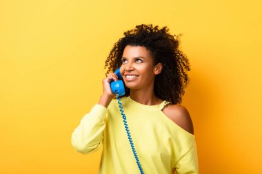Neşeli Afrikalı Amerikalı kadın sarıda klasik telefonla konuşuyor.