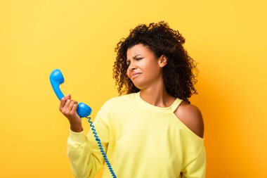 Üzgün Afrikalı Amerikalı kadın sarıdaki klasik telefona bakıyor.