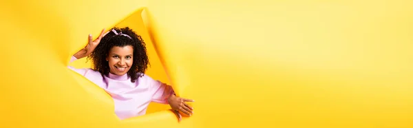 快乐的非洲裔美国女人用黄色背景 横幅撕破的纸片透过孔望着相机 — 图库照片