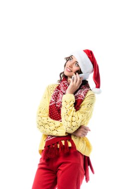 Noel Baba şapkalı ve atkılı neşeli genç bir kadın beyaz telefondan izole edilmiş bir şekilde konuşuyor. 