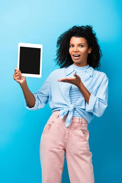 興奮したアフリカ系アメリカ人女性が青の上に空白の画面を持つデジタルタブレットで手を指して — ストック写真