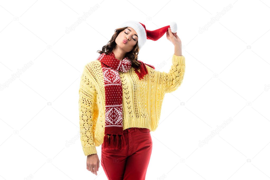 young woman with duck face and closed eyes touching santa hat isolated on white