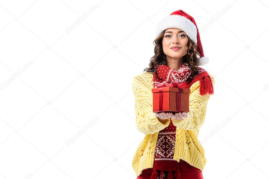 pleased woman in santa hat and red scarf holding present isolated on white