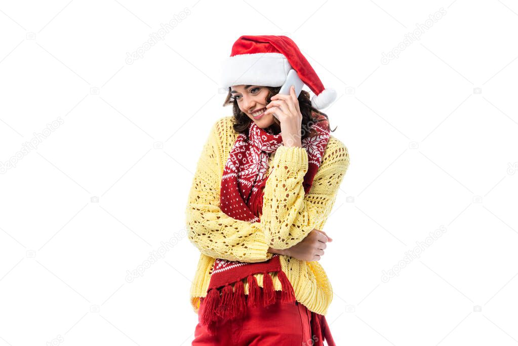 pleased young woman in santa hat and scarf talking on smartphone isolated on white 