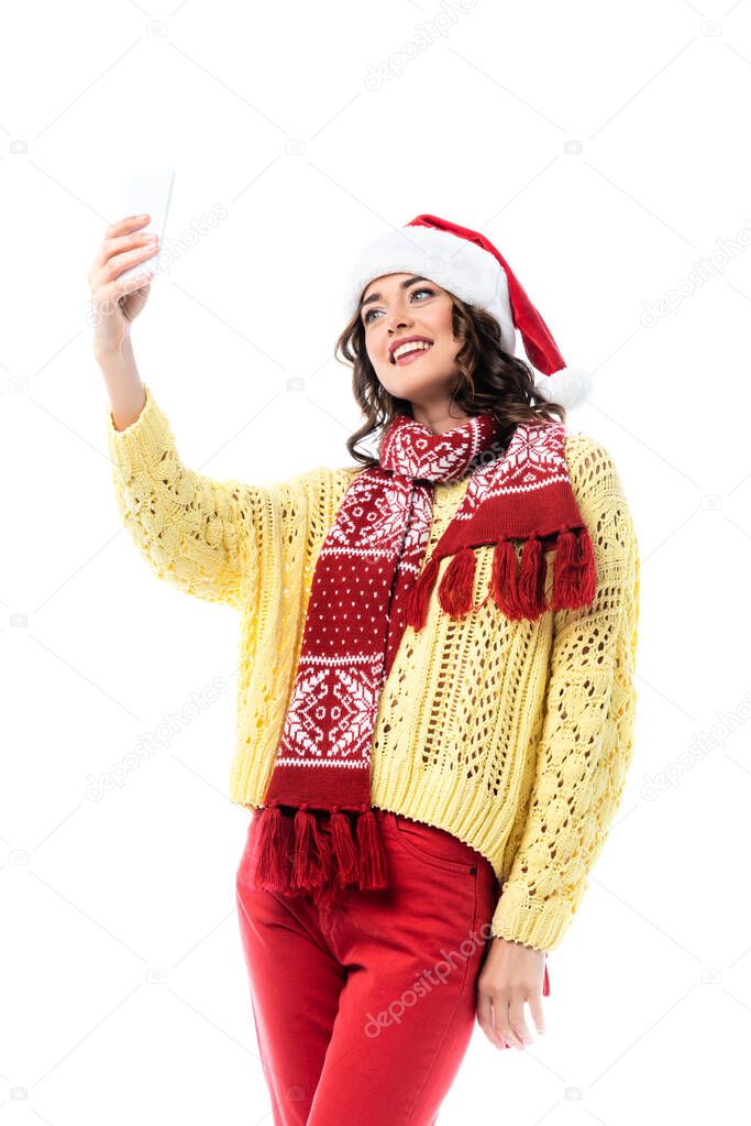 pleased woman in santa hat and scarf taking selfie on smartphone isolated on white 