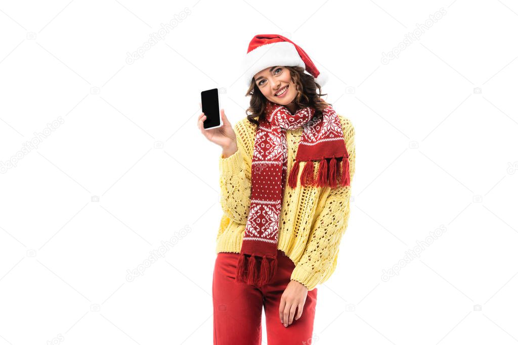 joyful young woman in santa hat and scarf holding smartphone with blank screen isolated on white 